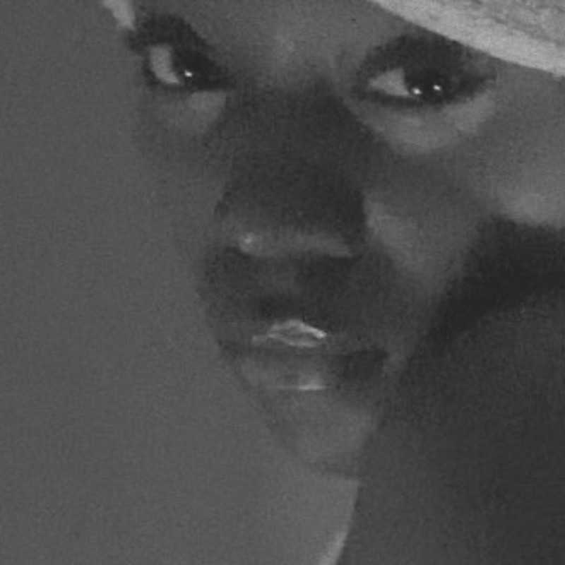 Celune is wearing a white head wrap and looking over her shoulder.